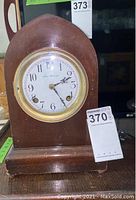 Full view of the wooden New Haven mantel clock showing arched top, rectangular base, round dial with white face and gold bezel.