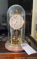 Full view of Kundo anniversary mantel clock with glass dome and brass base showing patina and clock hands.