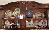 Full view of wooden cabinet containing assorted fine china plates, cups, bowls, salt and pepper shakers, and decorative ceramic items