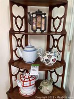 Overall view of five tea pots arranged on wooden corner shelf, includes Asian metal-framed painted tea pots and decorated ceramic tea pots