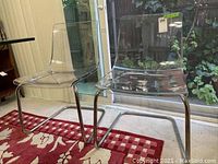 Side view of two transparent acrylic chairs showing clear acrylic seats and backrests with chrome tubular metal frames.