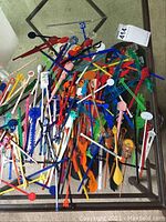 Photo showing a large pile of mixed colorful cocktail stirrers with various logos and designs on a glass table.
