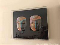 Photo showing the pair of Dominique Blanchard masks mounted on black backing with clear framing.