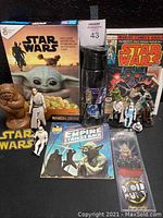 Photo showing the full lot including Star Wars comic book from 1977, Mandalorian cereal box, Empire Strikes Back record and read-along book, multiple action figures, water bottle, Ewok shampoo bottle, and Star Wars logo belt buckle.