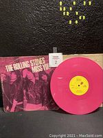 Pink vinyl record on black background next to its sleeve, showing both the bright pink color of the vinyl and the overall look of the album cover.