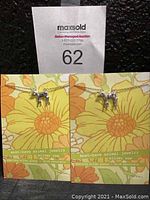 Pair of cow pendant necklaces on floral background cards showing brand and product details.