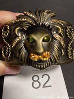 Photo of detailed lion face on wide cuff bracelet showing green rhinestones in eyes and orange/yellow rhinestones on mane and whiskers.
