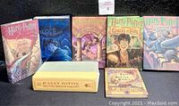 Seven hardcover books lined up: five with illustrated dust jackets, one main-series volume without jacket lying flat, and one smaller illustrated volume in front.