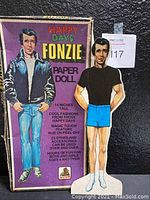 Photo of the original Happy Days Fonzie paper doll box with printed text and image of Fonzie character and additional doll figure standing next to it.