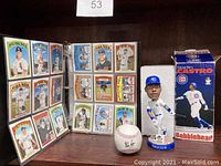 Photo showing open binder with vintage baseball cards, Starlin Castro bobblehead with box, and autographed Nolan Ryan baseball.