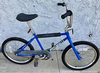 Side view of blue vintage Huffy Scrambler 20 kids bike showing frame, tires, seat, and handlebars.