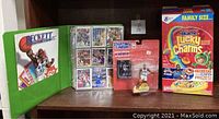 Photo showing Beckett magazine, basketball card binder, Starting Lineup Michael Jordan action figure in packaging, and Galactic Lucky Charms large cereal box on a wooden shelf.