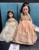 Photo showing both Madame Alexander dolls standing in front of vintage blue Madame Alexander box with pattern. Sarah Jackson doll in peach gown on right, Juliet doll in white gown on left.