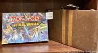 Image showing Monopoly Star Wars Saga Edition game box and vintage brown game case on a shelf.