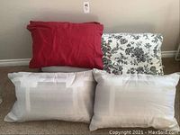 Four pillows in various pillowcases - red, black and white floral, and two white with subtle pattern