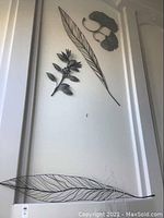 Four metal wall decor pieces arranged on a white wall: a large elongated leaf, a floral branch, a medium leaf, and two smaller ginkgo-shaped leaves.