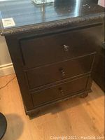Frontal view of black three-drawer nightstand showing carved trim and round knobs