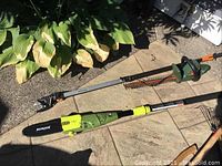 Fiskars pole pruner and Sunjoe electric pole chainsaw laid out on ground