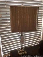 Front view of table lamp showing overall lamp with grey fabric shade in front of window blinds.