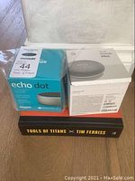 Photo of boxed Amazon Echo Dot, Google Home Mini, and Tim Ferriss Tools of the Titans book stacked