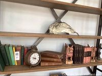 Wooden bookshelves holding various vintage and antique hardcover books, a vintage time clock, wooden carved bookends shaped like animals, and a vintage company seal.