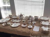 Wide view of full spread of plates, cups, mugs, serving pieces on table under window