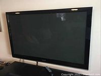 Front view of the Samsung 58-inch plasma HDTV, screen off with remote on the surface below.