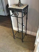 Full view of tall iron framed stand with stone top against wall.