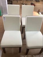 Front perspective view of four white upholstered dining chairs arranged