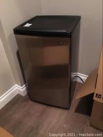 Full view of the Sanyo stainless steel bar fridge placed near corner walls on wood floor.