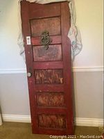 Front view of vintage wooden door, painted red with distressed finish and metal welcome sign mounted in center.