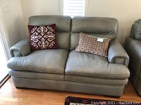Front view of grey leather loveseat with two decorative pillows, showing overall condition.