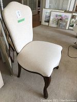 Side angle of cream coloured fabric accent chair showing upholstery and wooden legs.