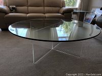 Full view of the round glass coffee table with a clear acrylic intersecting base in a living room.