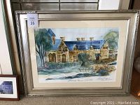 Framed watercolor painting of stone building with blue roof, signed by Susan Linggard, in a silver frame with double matting.
