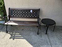 Bench with wooden slatted seat and lattice cast iron backrest alongside round metal side table