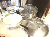 Multiple cookware items: Meyer pot with steamer insert and lid at center; Lagostina ceramic pans at left; metal baking pan behind