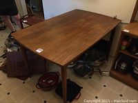 Overview of rectangular wooden table with four legs and drop leaves stored underneath