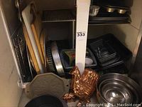 Photo showing multiple wooden cutting boards and metal baking trays stored together, along with copper hen-shaped mold and other pans on a shelf.