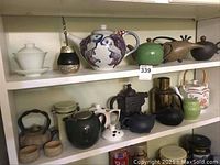 Two shelves displaying varied teapots and accessories against a white wall