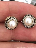 Front view of both round pearl and diamond halo stud earrings held in hand