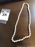 Full view of single-strand cultured pearl necklace laid out on wood surface, showing overall length and spacing