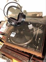 Overall view of turntable on wooden shelf with dust cover closed and Sony headphones on charging stand
