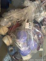Clear plastic bag containing multiple skeins of yarn including blue and beige colors and a partially knitted project.