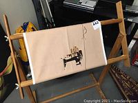 Wooden embroidery stand holding beige fabric with cross-stitch sewing machine design visible.