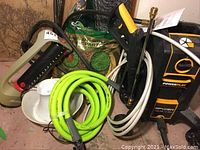 Full view of the lot showing pressure washer, hose, hedge trimmer, buckets, wire fencing, and packaged soil or seed.