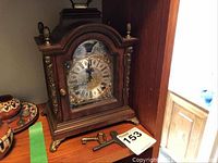 Front view of wooden case mantel clock with brass details and two keys laid in front