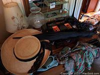 Photo showing two straw hats with black lace bands, black umbrella, scarves, and assorted accessories on wooden surface.