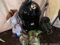 Full view of smoker with thermometer, charcoal bags, wood chips and chimney starter