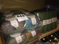 Assorted plastic-wrapped yarn packs on shelf showing multicolor Rhythm and solid green skeins
